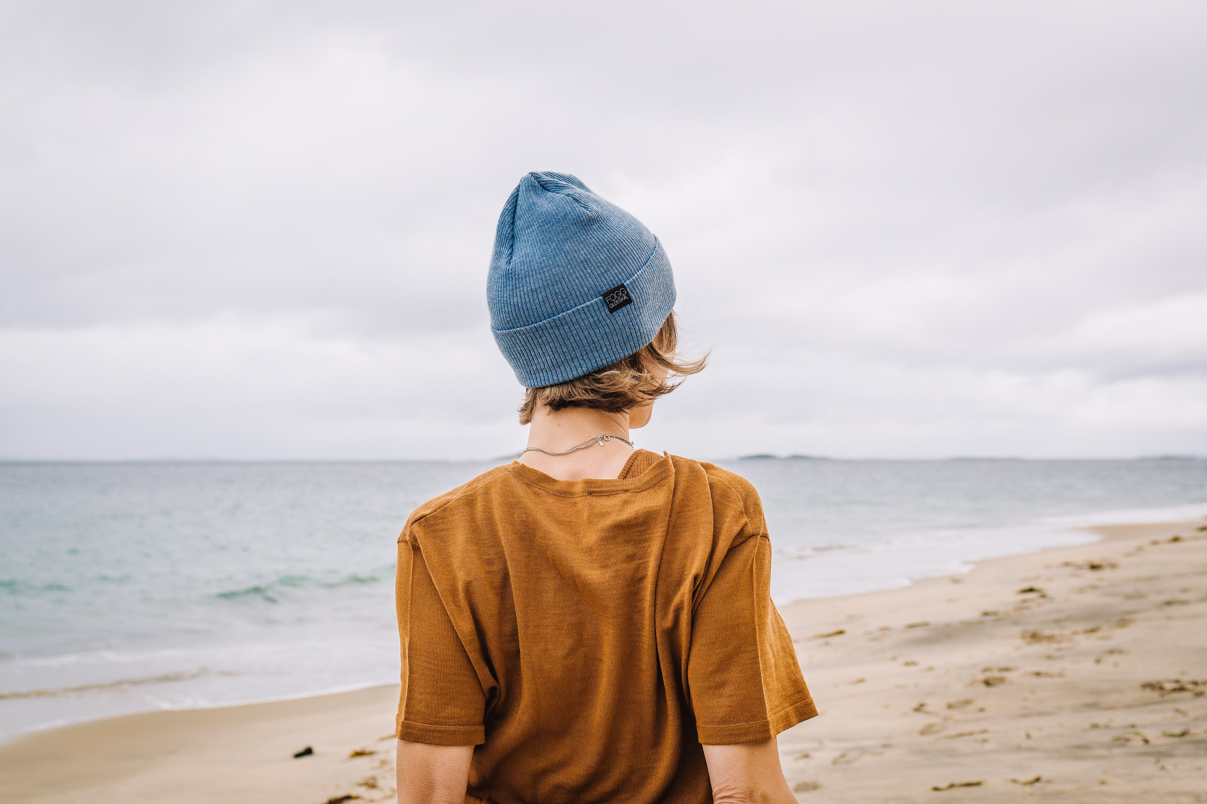 Woman standing on northern beach wearing a light blue beanie and a woollen t-shirt